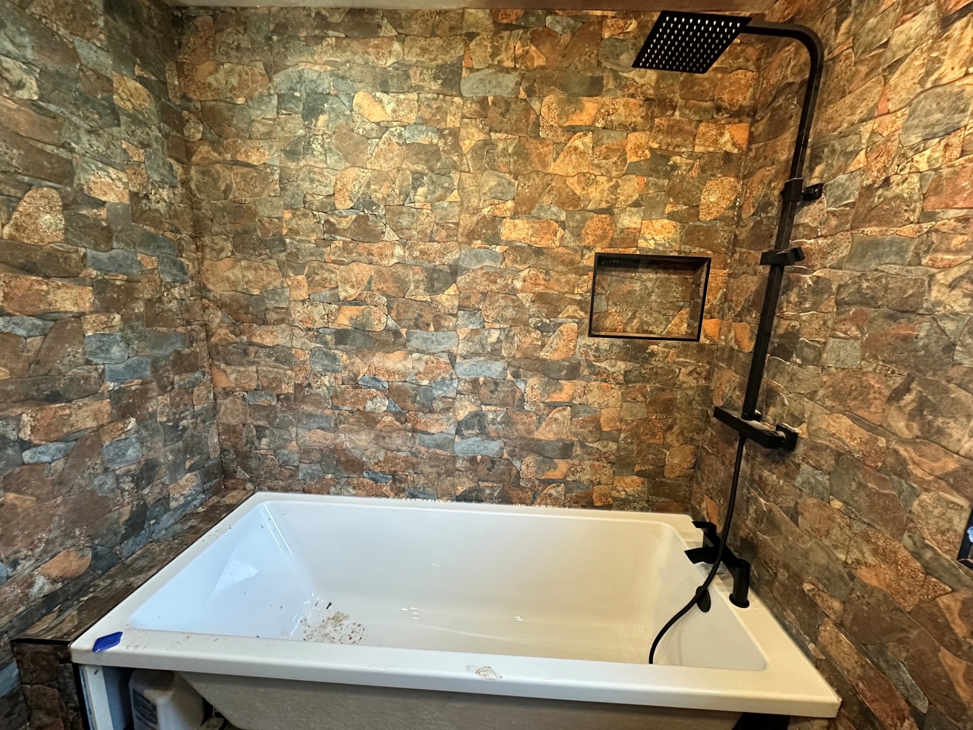 Deep soaker tub with matt black rainfall shower & stone-clad walls