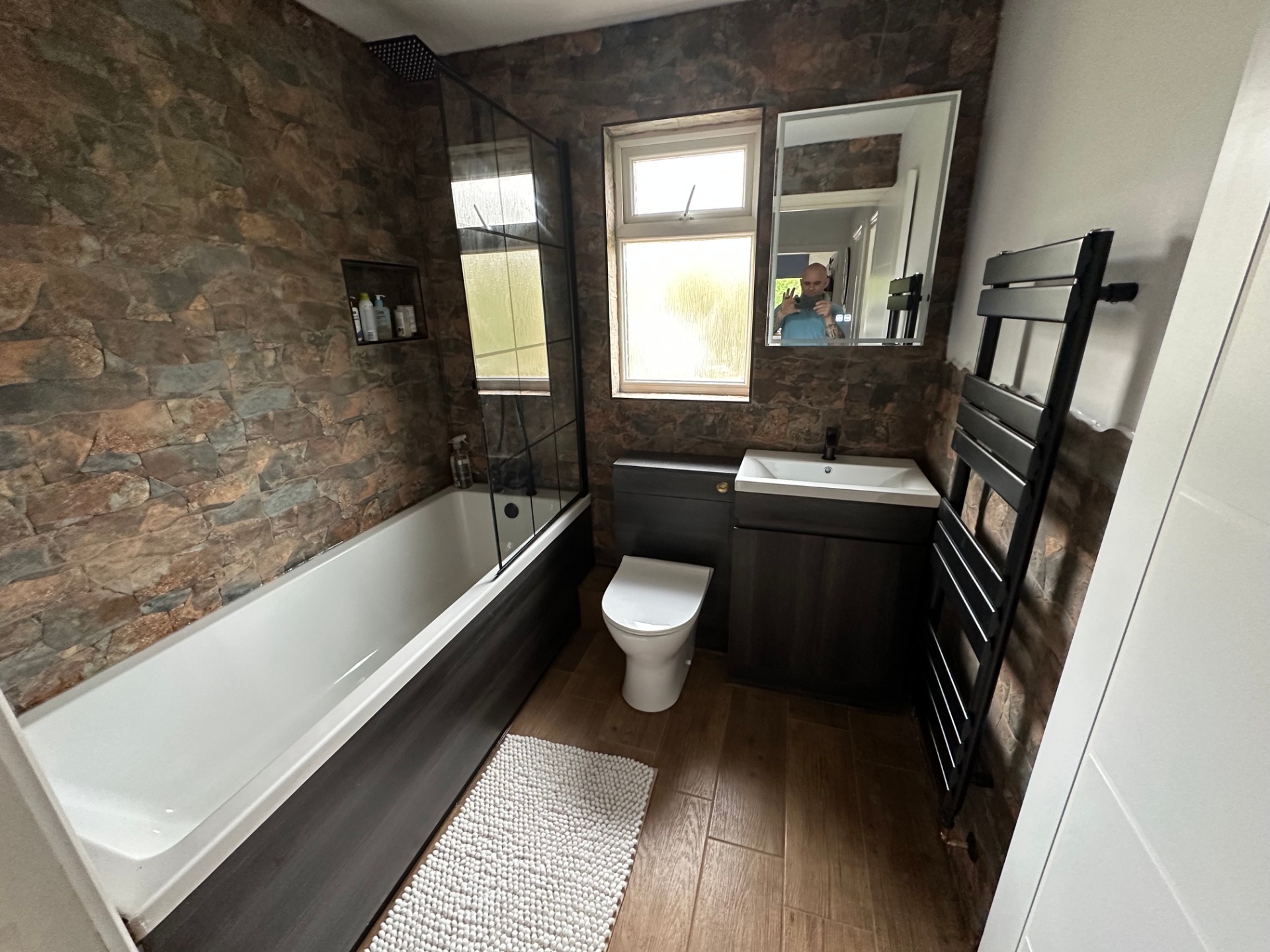 Stripped-back room → stone-clad bath with matt black fittings — after